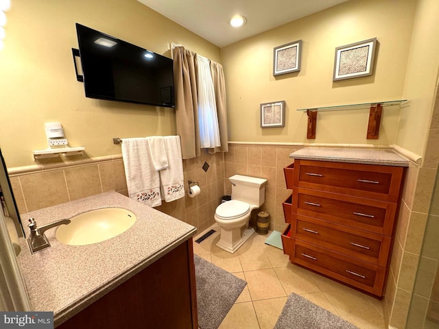 bathroom featuring tile patterned flooring, tile walls, toilet, wainscoting, and vanity