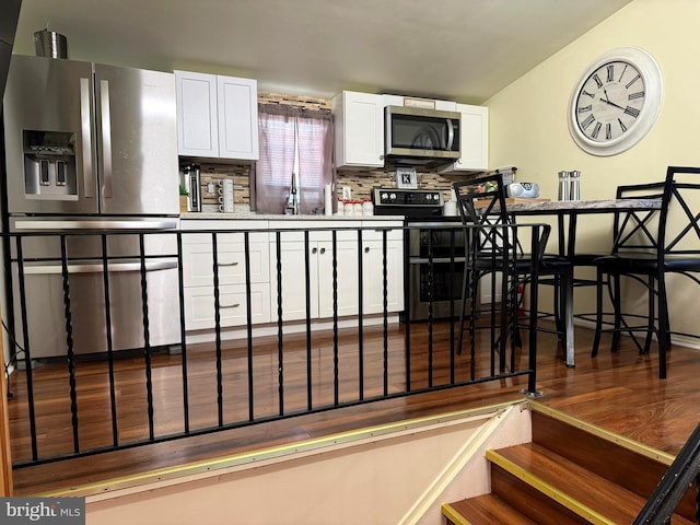 kitchen featuring a sink, tasteful backsplash, wood finished floors, white cabinetry, and stainless steel appliances