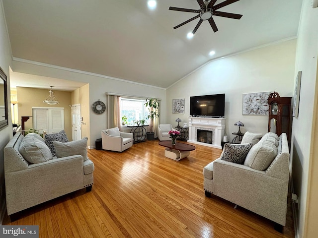 living room featuring ornamental molding, vaulted ceiling, a fireplace, light wood-style floors, and a ceiling fan