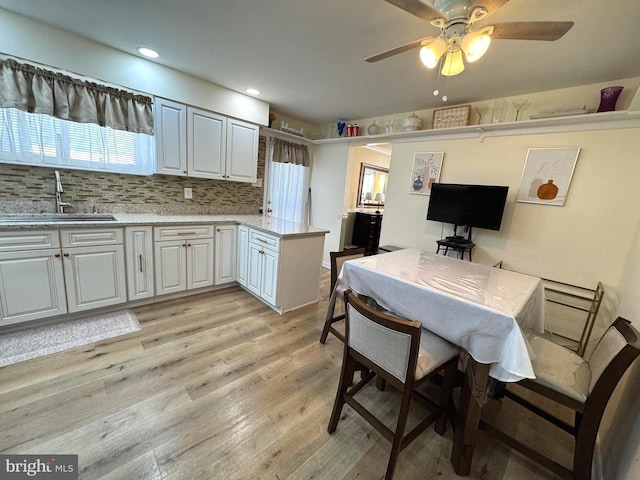 kitchen with tasteful backsplash, light wood-style flooring, a peninsula, white cabinets, and a sink