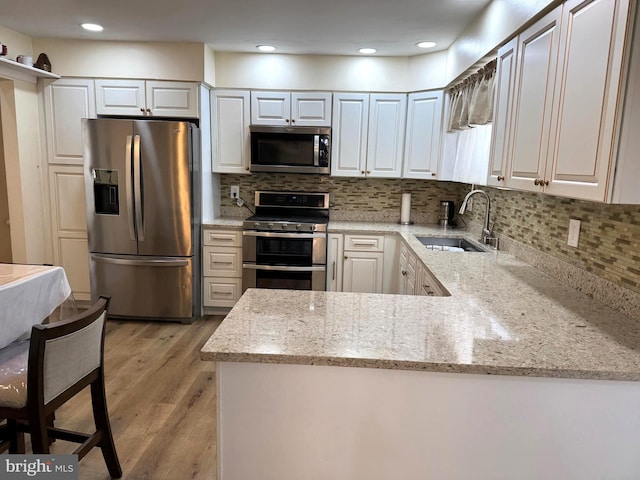 kitchen featuring light stone countertops, light wood-style floors, white cabinets, stainless steel appliances, and a sink