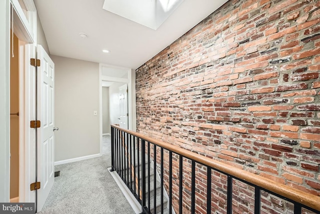 hallway with light carpet, brick wall, and a skylight