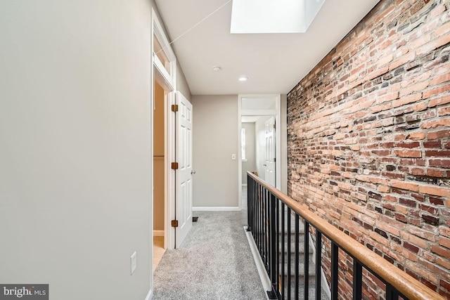 hallway with light colored carpet, brick wall, and a skylight