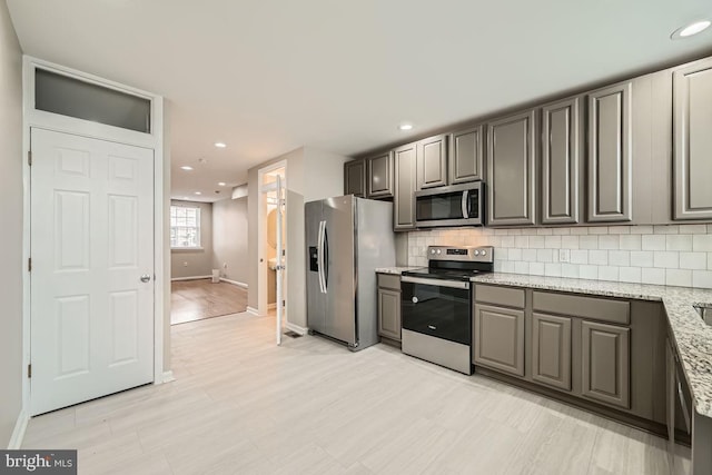 kitchen with appliances with stainless steel finishes, gray cabinets, tasteful backsplash, and light stone counters