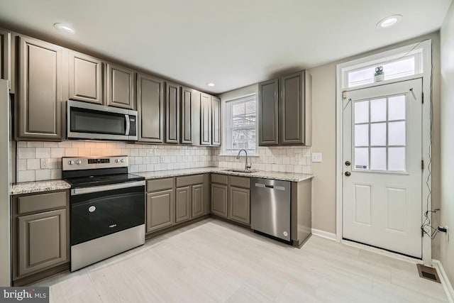 kitchen with light stone countertops, backsplash, stainless steel appliances, and sink