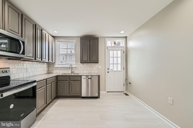 kitchen featuring a wealth of natural light, sink, light stone countertops, and appliances with stainless steel finishes