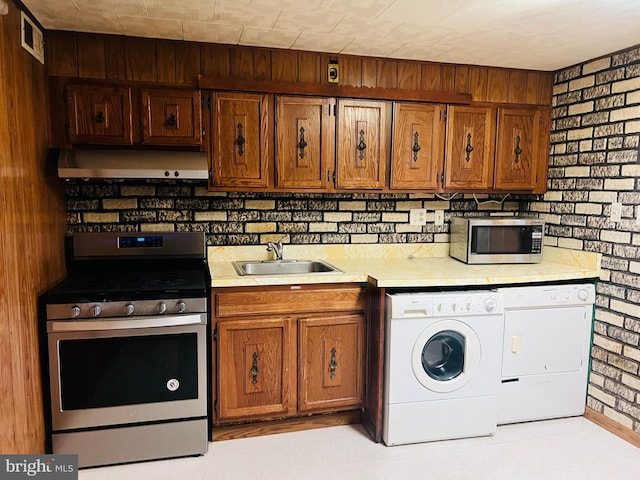 kitchen with independent washer and dryer, sink, brick wall, and appliances with stainless steel finishes