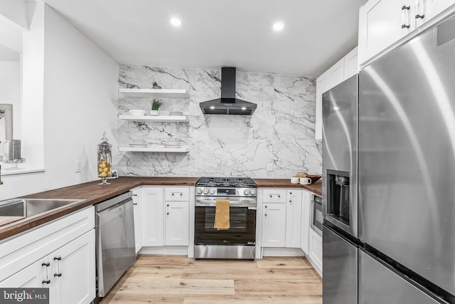 kitchen with white cabinets, wall chimney exhaust hood, appliances with stainless steel finishes, tasteful backsplash, and butcher block countertops