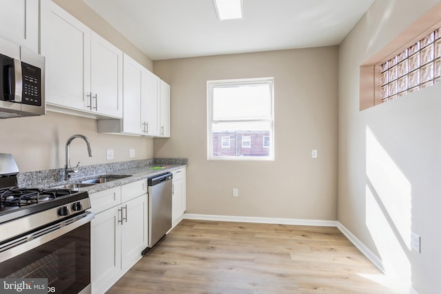 kitchen with light stone countertops, stainless steel appliances, sink, white cabinets, and light hardwood / wood-style floors