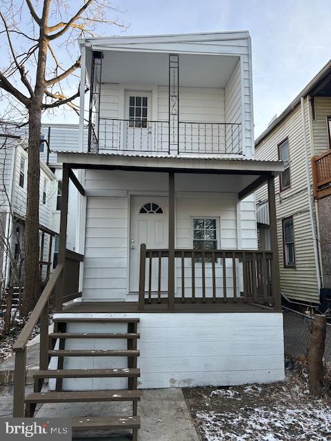 snow covered rear of property with covered porch and a balcony