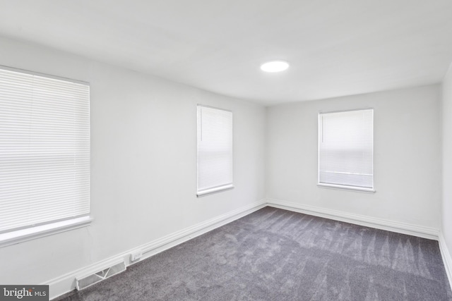 spare room featuring a wealth of natural light and dark carpet