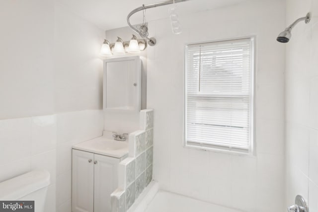 bathroom with a tile shower, vanity, toilet, and tile walls