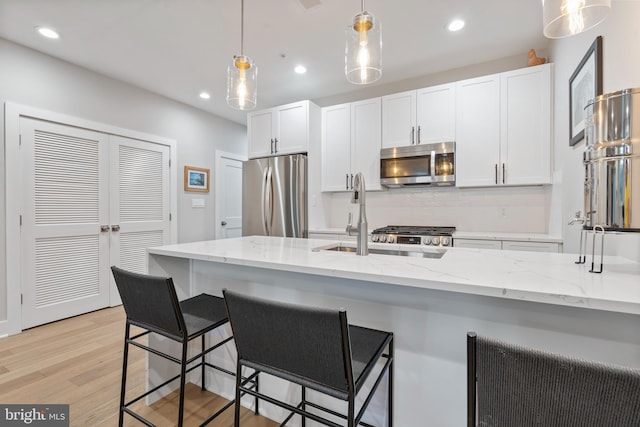 kitchen featuring white cabinets, hanging light fixtures, light wood-type flooring, light stone countertops, and stainless steel appliances