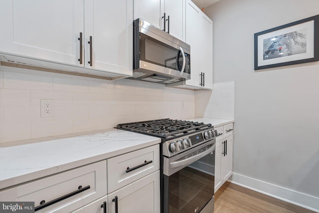 kitchen with light stone countertops, appliances with stainless steel finishes, light wood-type flooring, backsplash, and white cabinets