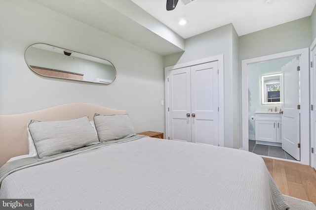 bedroom with sink, ensuite bath, ceiling fan, light wood-type flooring, and a closet