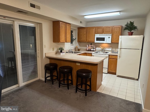 kitchen featuring white appliances, visible vents, a breakfast bar area, a peninsula, and a sink