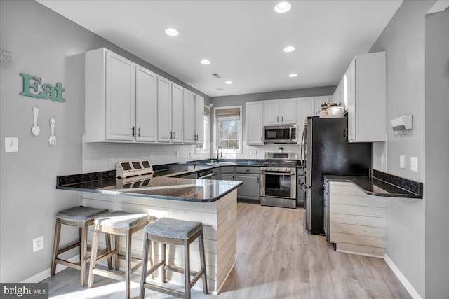 kitchen featuring a kitchen breakfast bar, kitchen peninsula, white cabinets, and appliances with stainless steel finishes