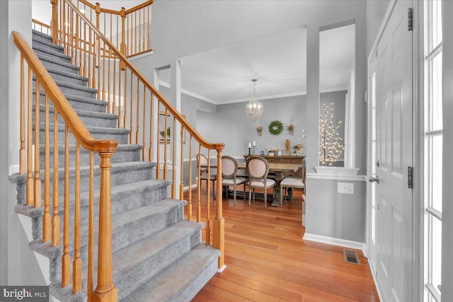 stairs with crown molding, an inviting chandelier, and hardwood / wood-style flooring