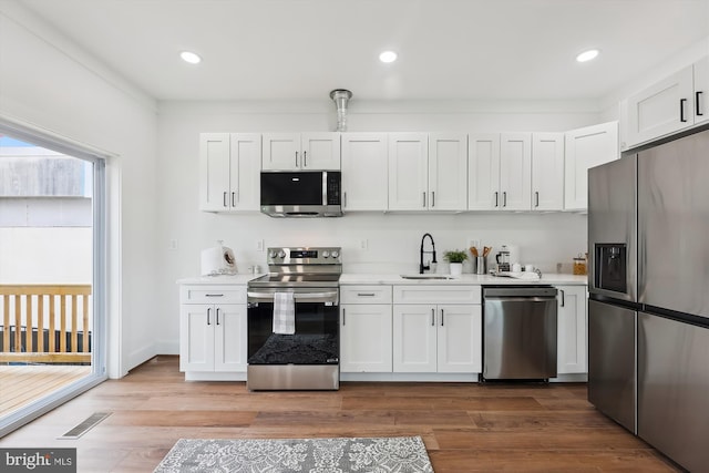 kitchen featuring white cabinetry, sink, crown molding, hardwood / wood-style floors, and appliances with stainless steel finishes