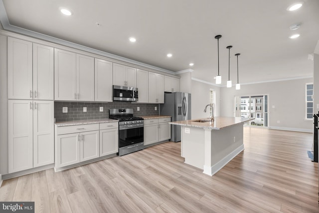 kitchen featuring light stone counters, ornamental molding, hanging light fixtures, a center island with sink, and appliances with stainless steel finishes