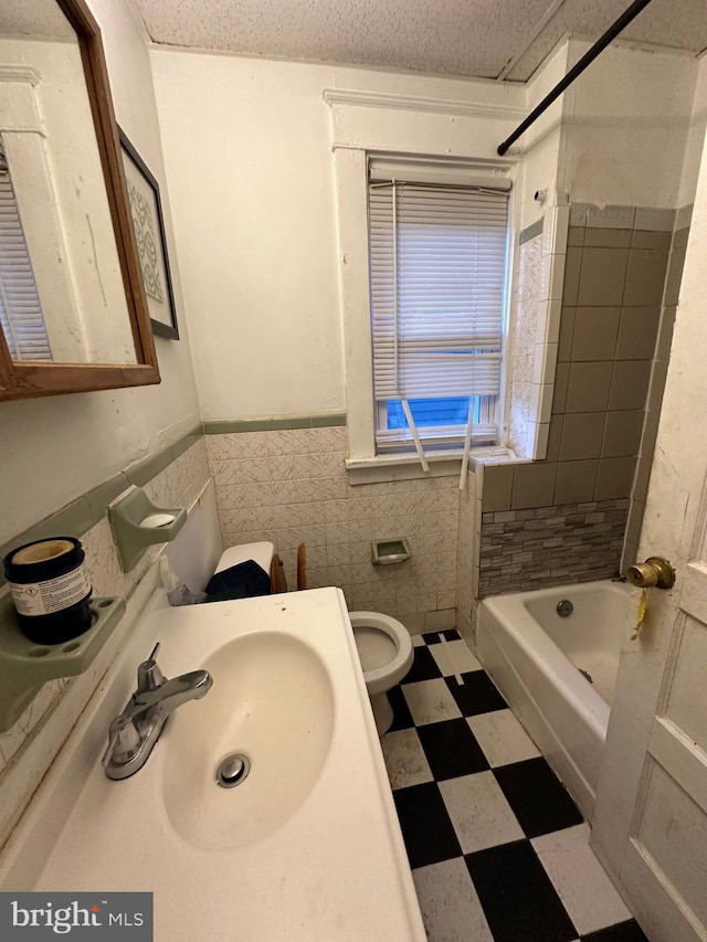 full bathroom with a textured ceiling, sink, tile walls, toilet, and tiled shower / bath