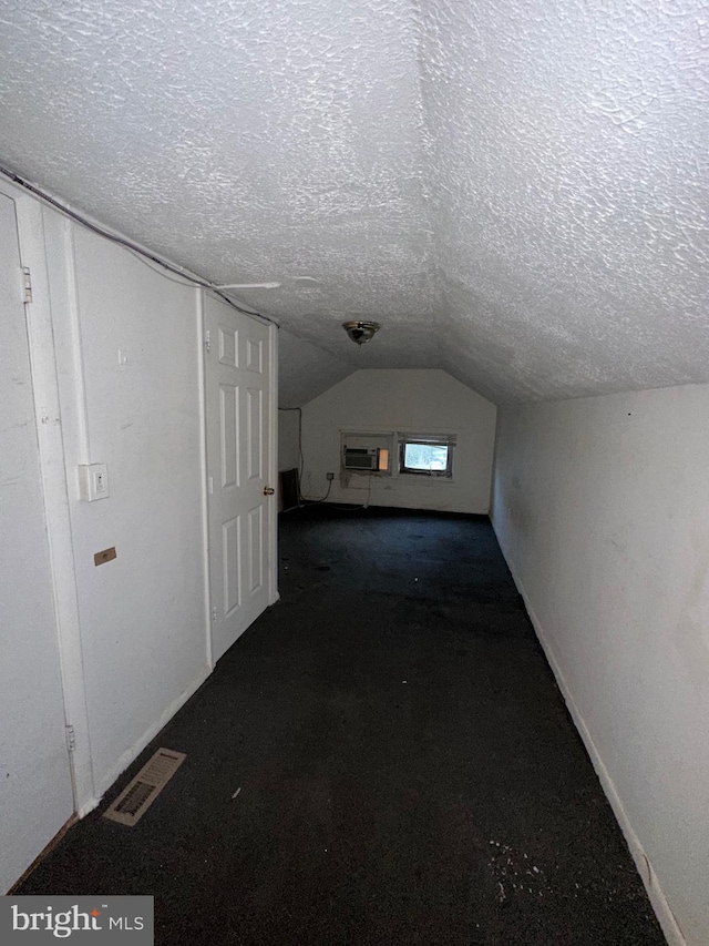 bonus room featuring dark carpet, lofted ceiling, a textured ceiling, and a wall mounted AC