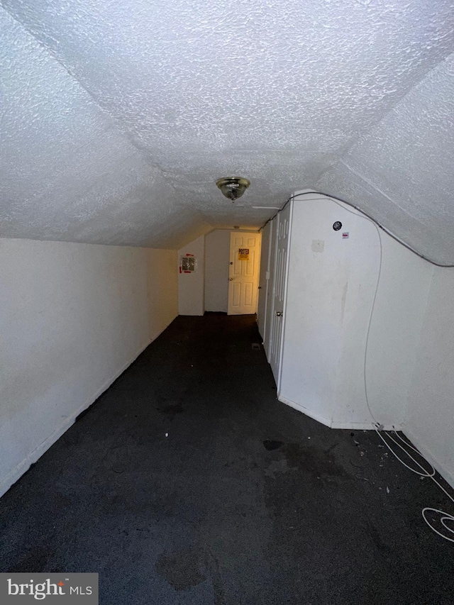 bonus room with dark colored carpet, lofted ceiling, and a textured ceiling