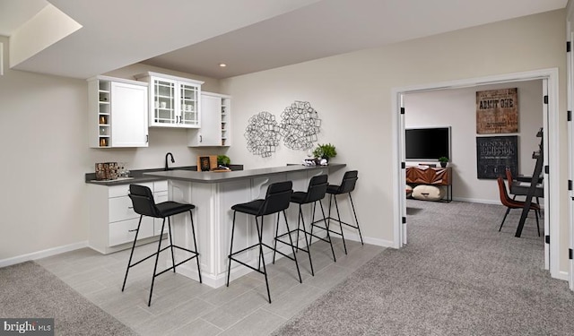 kitchen featuring light carpet, a kitchen bar, kitchen peninsula, sink, and white cabinets