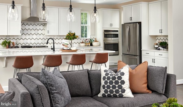 kitchen with backsplash, wall chimney exhaust hood, stainless steel appliances, decorative light fixtures, and white cabinetry