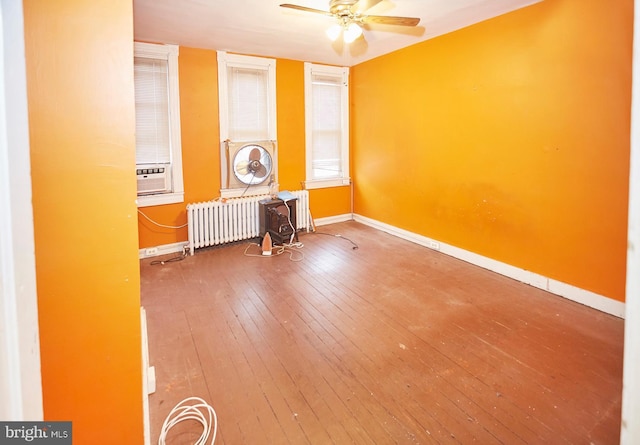 spare room with ceiling fan, cooling unit, hardwood / wood-style flooring, radiator heating unit, and a wood stove