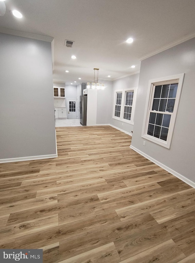 unfurnished living room with an inviting chandelier, light wood-type flooring, and ornamental molding