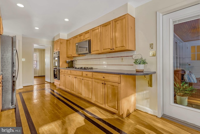 kitchen featuring stainless steel appliances, light hardwood / wood-style flooring, light brown cabinetry, and backsplash