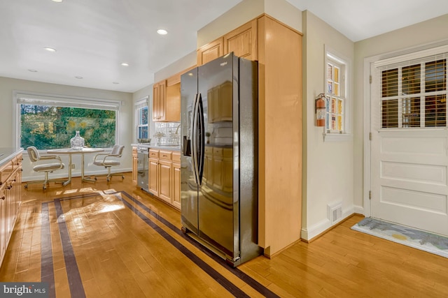 kitchen with light wood-type flooring, black fridge with ice dispenser, stainless steel dishwasher, and light brown cabinets