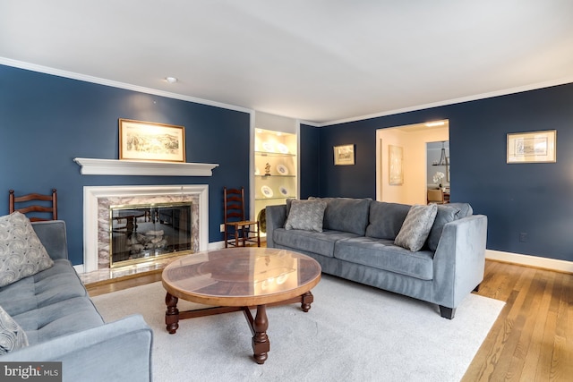 living room with ornamental molding, light wood-type flooring, a high end fireplace, and built in shelves