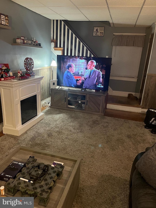 living room featuring carpet flooring, a paneled ceiling, and wooden walls