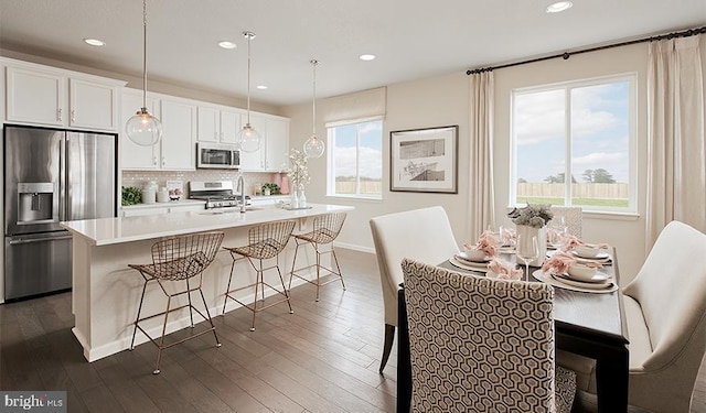 kitchen featuring white cabinetry, a center island with sink, stainless steel appliances, and decorative light fixtures