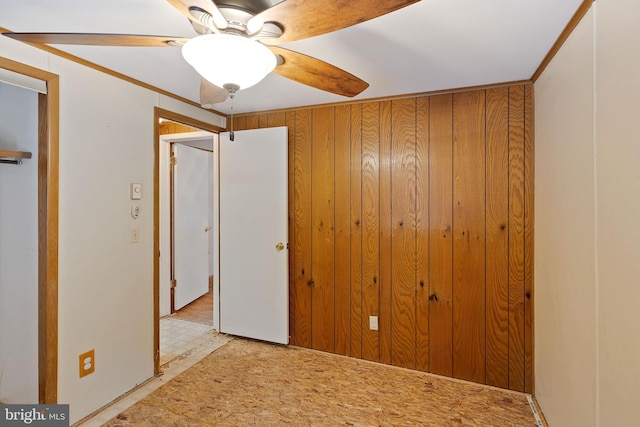 unfurnished bedroom with ceiling fan, wood walls, and ornamental molding