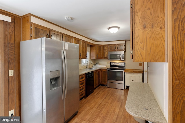 kitchen with light stone countertops, ornamental molding, stainless steel appliances, sink, and light hardwood / wood-style flooring