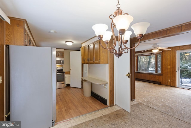 kitchen with pendant lighting, wood walls, ceiling fan with notable chandelier, baseboard heating, and stainless steel appliances