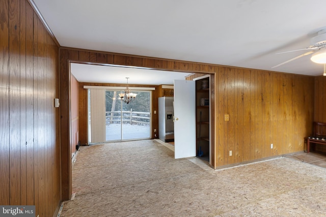 carpeted spare room featuring ceiling fan with notable chandelier and wooden walls