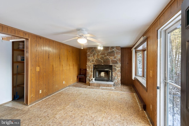 unfurnished living room with a fireplace, ceiling fan, and wooden walls