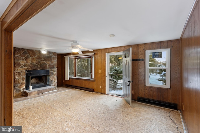 unfurnished living room featuring ceiling fan, wood walls, a stone fireplace, and a baseboard radiator