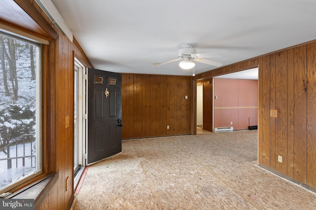 empty room featuring ceiling fan, a baseboard radiator, and wood walls