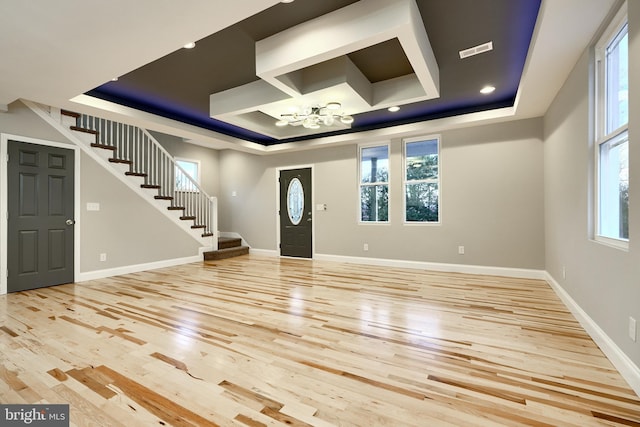 foyer with light wood-type flooring, a tray ceiling, and an inviting chandelier