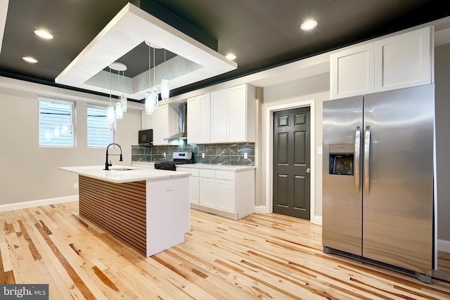 kitchen with appliances with stainless steel finishes, wall chimney exhaust hood, a center island with sink, decorative light fixtures, and white cabinetry