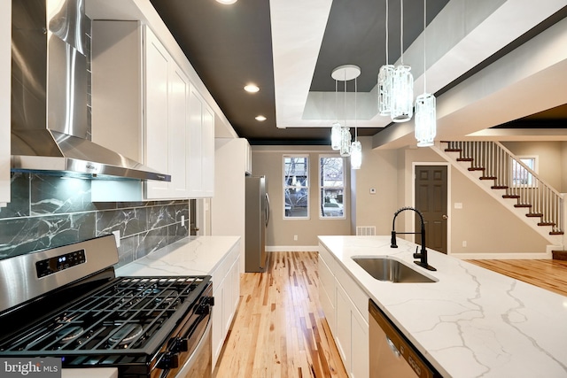 kitchen featuring stainless steel appliances, sink, wall chimney range hood, white cabinetry, and hanging light fixtures