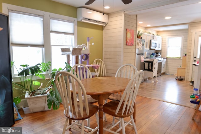 dining room with wooden walls, ceiling fan, a wall mounted air conditioner, and light hardwood / wood-style flooring