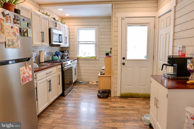 kitchen featuring stainless steel appliances, wooden walls, white cabinetry, light hardwood / wood-style floors, and beam ceiling