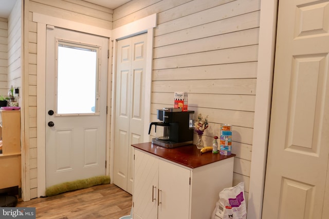 doorway to outside with light wood-type flooring and wood walls