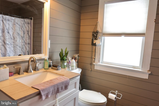 bathroom with toilet, wood walls, a wealth of natural light, and vanity